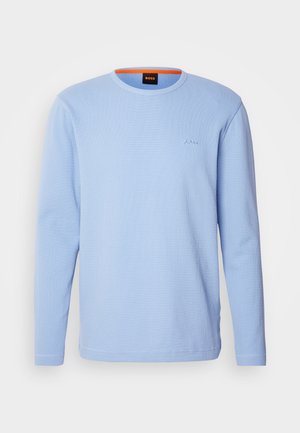 Šviesiai mėlynas ilgomis rankovėmis marškinėliai, pagaminti iš tekstūruotos medžiagos, su banguota iškirpte ir siuvinėtu logotipu ant krūtinės tos pačios spalvos.