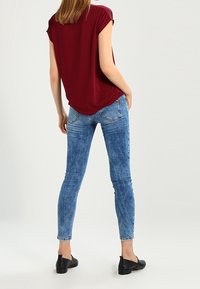 Top corto de manga corta en color marrón con un corte relajado, combinado con unos vaqueros ajustados de color azul. Los vaqueros presentan una textura de denim deslavado y un acabado mate suave. Zapatos planos negros.