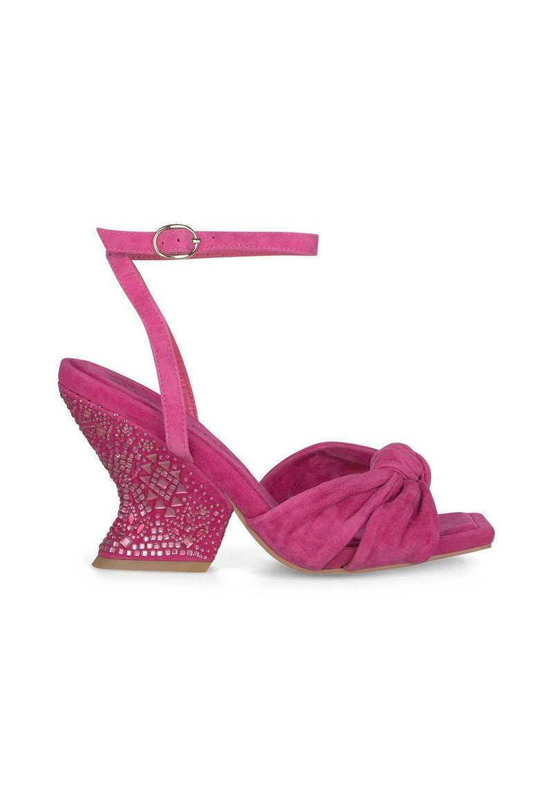 Fuksjowe zamszowe sandały na koturnie z wiązanym paskiem na palcach oraz teksturowanym geometrycznym wzorem w wycięciach na obcasie. Regulowany pasek na kostkę.