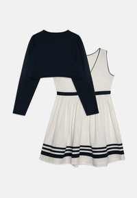 Top de manga larga azul marino superpuesto a un vestido crema, con falda acampanada que presenta rayas azul marino en el dobladillo y un diseño de escote en V.