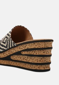 Gros plan d'une sandale compensée avec tige tissée noire et blanche et semelle en liège avec des rayures noires et une surface texturée.