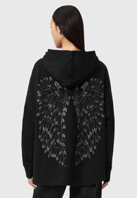 Fekete kapucnis pulóver, nagy ezüstszárny mintával a háton, puha anyagból készült, laza szabással.