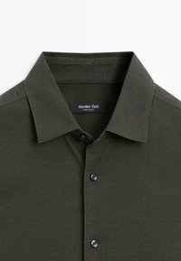 Donkergroene overhemdbloes gemaakt van een textuurstof, met een zachte kraag en zwarte knopen, met een label dat "Massimo Dutti" leest.