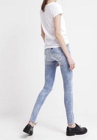 Jeans skinny de un azul claro deslavado con una textura desgastada, combinados con una camiseta blanca de manga corta y zapatos negros con cordones.