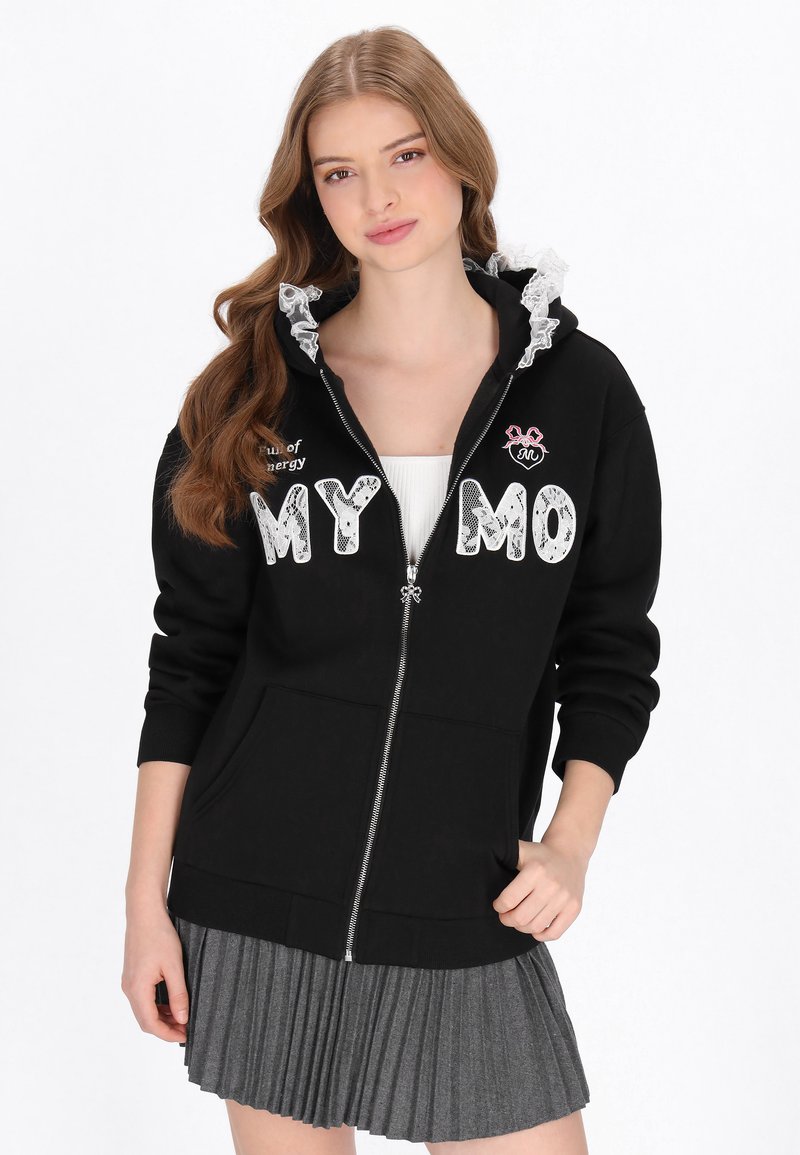 Sudadera negra con cremallera y capucha con borde de encaje, con la inscripción "MY MO" en letras blancas y un pequeño emblema rosa. Combinada con una falda gris plisada.