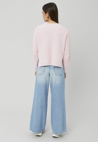 Pull rose pâle en tricot avec ourlet côtelé associé à un jean en denim bleu délavé à jambes larges. Baskets blanches et silhouette lisse et décontractée.