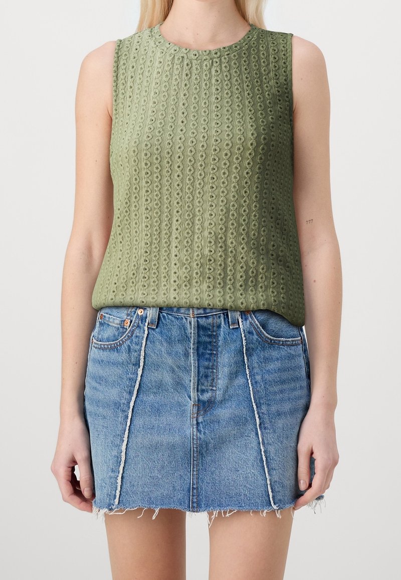Haut sans manches vert olive en tricot ajouré associé à une mini-jupe en denim bleu avec des coutures verticales effilochées et un ourlet brut.