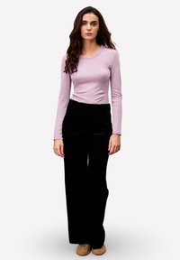 Haut à manches longues de couleur violet clair associé à un pantalon en velours côtelé noir taille haute. La tenue présente un design ajusté et une texture douce.