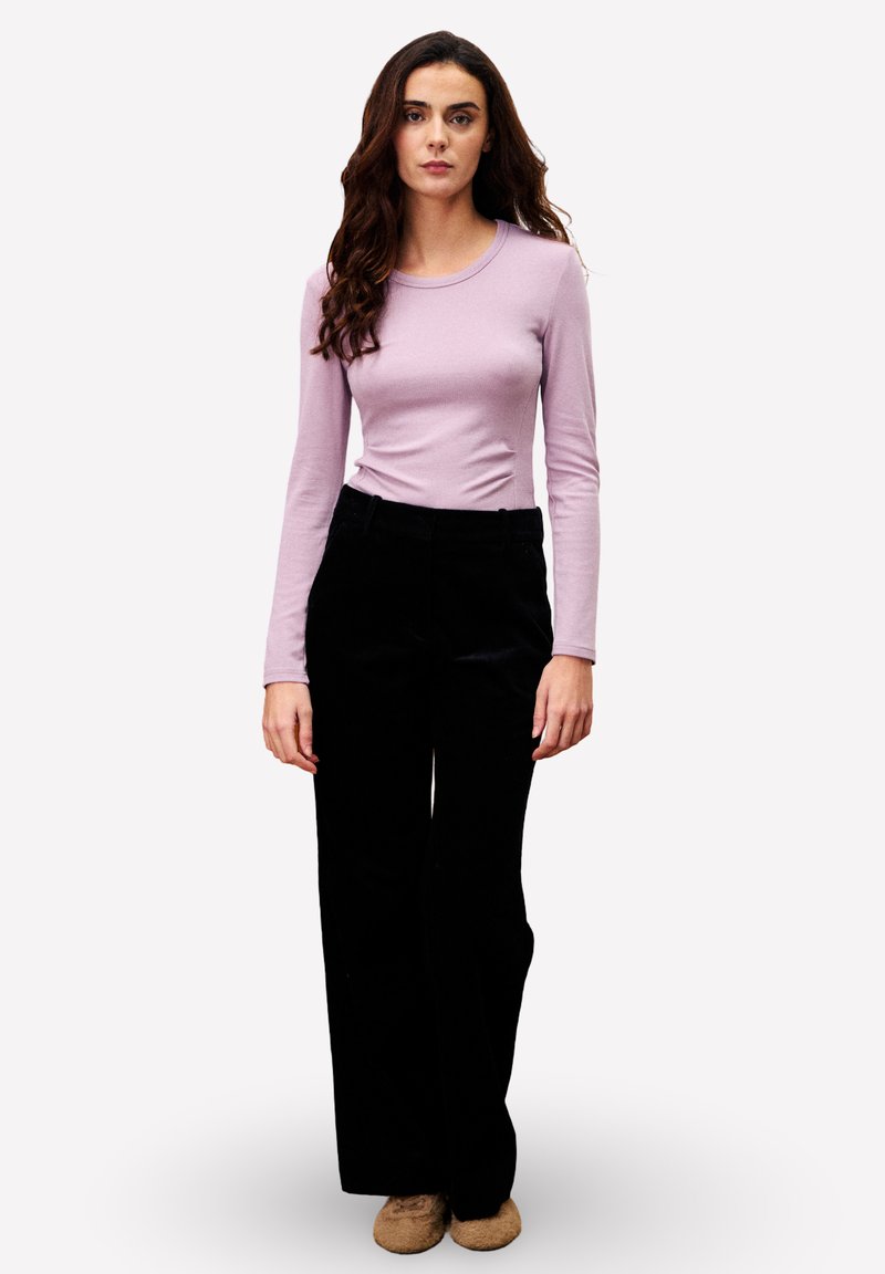 Haut à manches longues de couleur violet clair associé à un pantalon en velours côtelé noir taille haute. La tenue présente un design ajusté et une texture douce.