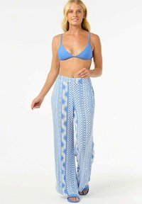 Blaue gerippte Bikini-Oberteile kombiniert mit weit geschnittenen Hosen, die mit einem blau-weißen Muster aus Karos und floralen Designs versehen sind. Blaue flache Sandalen.