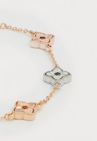Ein Armreif aus Roségold und Silber mit drei strukturierten, blütenförmigen Akzenten, die durch eine zarte Kette verbunden sind. Der Armreif zeigt abwechselnde Farben und Muster.