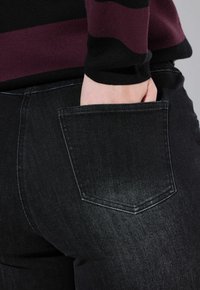 Jeans in denim nero con una tasca posteriore, visti di lato. Il tessuto è testurizzato, leggermente sbiadito e presenta un design a calzata moderna.