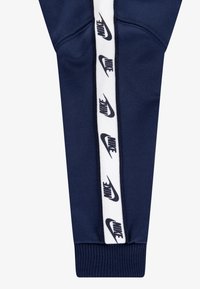 Ναυτικά αθλητικά παντελόνια με εφαρμοστή γραμμή, που διαθέτουν λευκή πλευρική ρίγα με επαναλαμβανόμενα μαύρα λογότυπα Nike, ριμπ μανσέτες και λεία υφή.