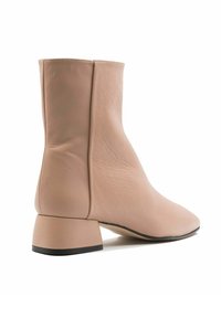 Botín beige de tobillo hecho de cuero suave, con tacón de bloque y punta afilada. El diseño tiene costuras mínimas y una silueta elegante.