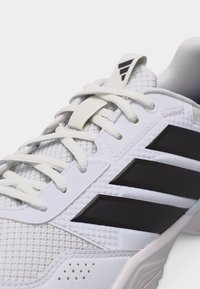 Λευκό αθλητικό παπούτσι με μαύρες ρίγες Adidas, λευκά κορδόνια και υφασμάτινη πλέξη με υφή στο επάνω μέρος.