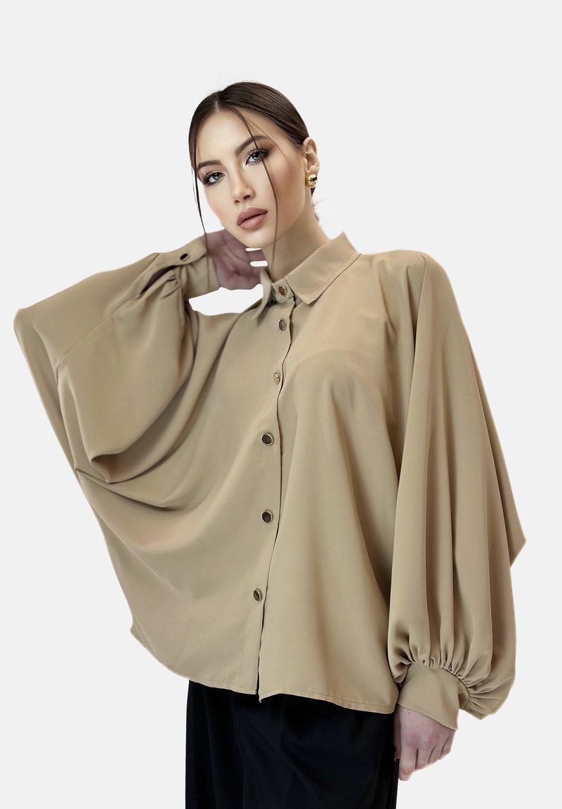 Tan oversized shirt gemaakt van gladde stof; heeft een button-up voorkant, luchtige mouwen en verzamelde manchetten voor extra detail.