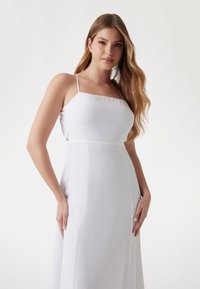 White dress with spaghetti straps, square neckline, and a flowing silhouette. Features side cutouts and smooth, lightweight fabric.