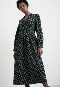 Langarm, v-hals jurk van donkere stof met een bloemenprint in crème en groen. Heeft een taillerende taille en een uitlopende rok. Zachte textuur.