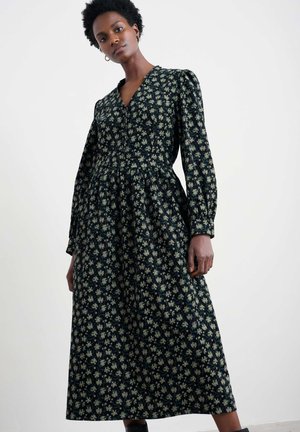 Langarm, v-hals jurk van donkere stof met een bloemenprint in crème en groen. Heeft een taillerende taille en een uitlopende rok. Zachte textuur.