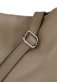 Ronde lederen handtas in taupe, met een getextureerde afwerking. Geaccentueerd met een zilverkleurige metalen gesp en bijpassende stiksels op de riem.