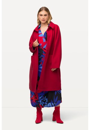 Red wool coat with oversized fit, featuring a collar, two front pockets, and a single button. Underneath is a floral-patterned dress in blue and red.