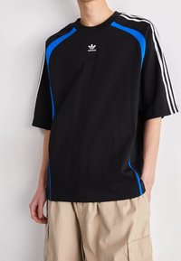 Černé tričko s krátkým rukávem a modrými akcenty, na rukávech se třemi bílými pruhy. Má vyšívané logo Adidas na hrudi.