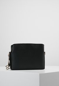 Svart syntetisk handväska med en texturerad yta, har en guldkedjeaccent och dragkedjestängning. Rektangulär form med en platt botten.