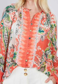 Bluse mit floralen Mustern in Korallen- und Grüntönen, ausgestattet mit einer durchgehenden Knopfleiste mit runden Knöpfen und langen Ärmeln. Hergestellt aus leichtem Stoff.
