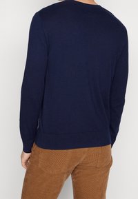 Mörkblå stickad tröja med långa ärmar, rund halsringning och ribbstickad nederkant. Bärs med bruna manchesterbyxor, vilket ger en avslappnad stil.