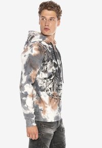 Hoodie im Batikdesign in Grau, Weiß und Braun mit einem Schädelgrafik und Kettendetails. Verfügt über eine Kapuze mit Kordelzug und gerippte Bündchen.