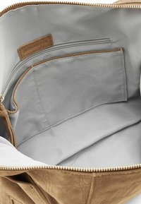 Interno di borsa in pelle scamosciata color cuoio con fodera in tessuto grigio chiaro e liscio. Presenta una tasca con zip e un'etichetta con la scritta "FredsBruder".