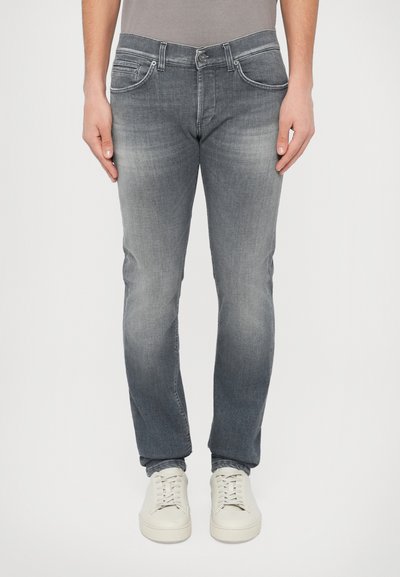 Jean denim gris à coupe slim, avec cinq poches, légère décoloration et une fermeture éclair classique, porté avec des baskets blanches.