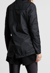 Veste rembourrée noire avec un col haut, présentant une texture lisse, des manches longues et un ourlet arrière légèrement plus long pour un meilleur confort.