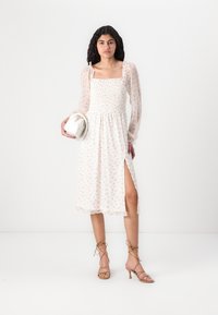 Rochie midi florală cu decolteu pătrat, corset elastic, mâneci balloon transparente și fenta laterală. Material ușor cu accente roz și verzi.