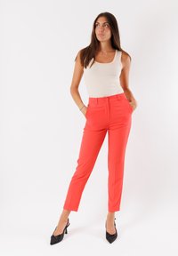 Pantaloni rossi su misura realizzati in tessuto morbido, con tasche laterali, chiusura a bottone e un design slim fit.