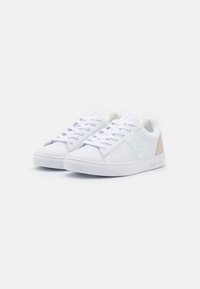 Sneakers bianche con texture in pelle liscia, dotate di lacci, dettagli perforati sulla punta e un accento beige a contrasto sul tallone.
