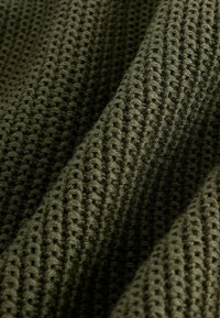 Tissu tricoté vert olive avec un tissage texturé, mettant en valeur un motif de sections surélevées et creuses, créant un aspect dimensionnel.