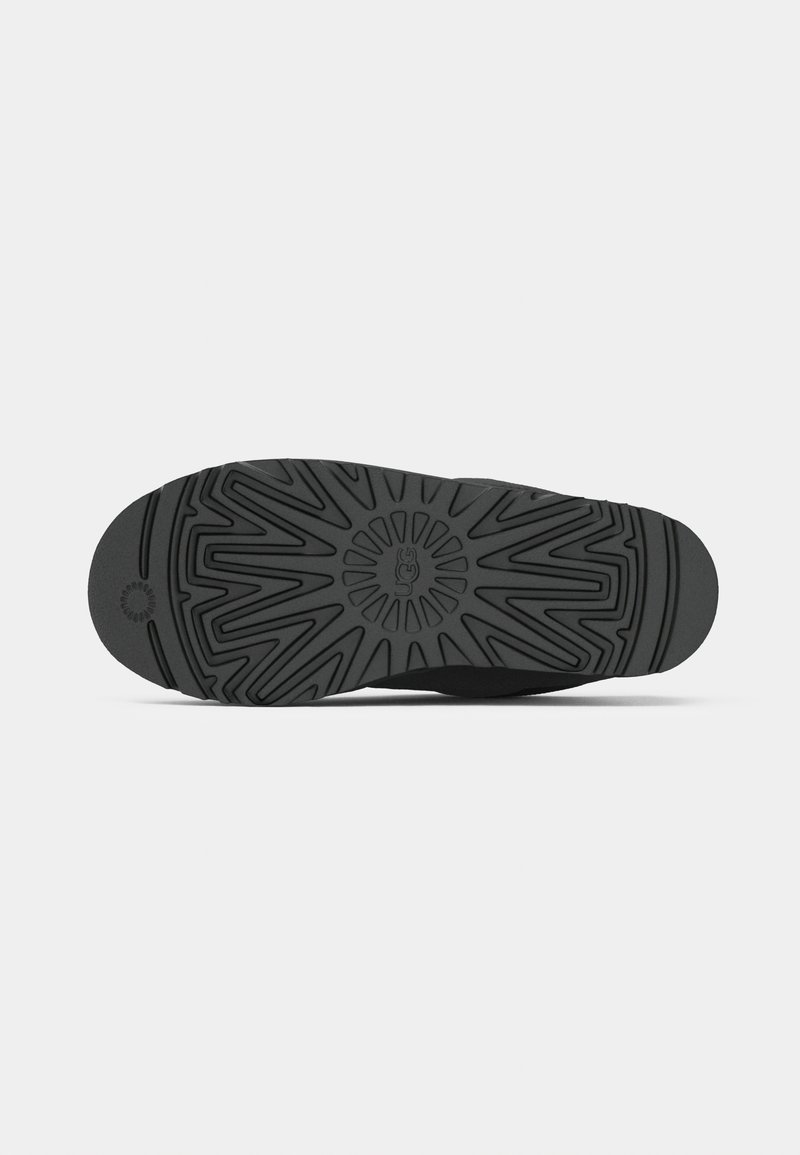 Suela de goma negra con un patrón de tracción detallado, superficie lisa y un logo circular en el centro.