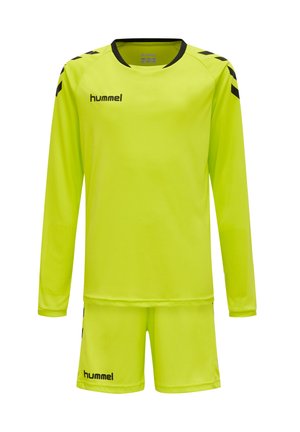 Camiseta deportiva de manga larga y pantalones cortos de color amarillo brillante con logo negro de hummel y detalles en forma de chevrones en los hombros y las mangas.