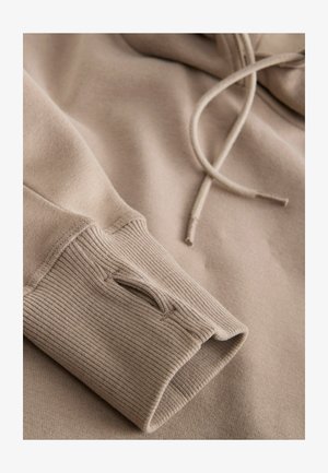 Beige hoodie with ribbed cuffs and a textured finish. Drawstrings at the neck and a soft, smooth fabric. Subtle stitching details.