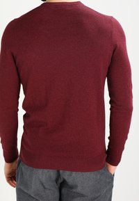 Burgunderfarbener Strickpullover mit rundem Ausschnitt, gerippten Manschetten und Saum; verfügt über eine glatte Textur und eine taillierte Passform.