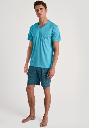 Türkises Baumwoll-V-Ausschnitt-T-Shirt mit einer Brusttasche, kombiniert mit blauen gemusterten Shorts mit hellblauen Akzenten.