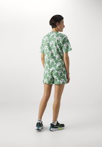 Pantalones cortos verdes con estampado y camisa de manga corta a juego, hechos de una tela ligera, que presenta un diseño de hojas sobre un fondo blanco.