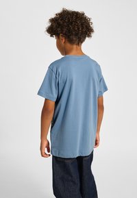 Blå bomulls-t-shirt med korta ärmar, rund halsringning och avslappnad passform, sedd bakifrån, tillsammans med mörka jeans.