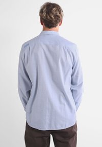 Chemise à manches longues bleu clair avec un col boutonné, texture douce et étiquette au dos de l'épaule. Ourlet droit avec coupe décontractée.