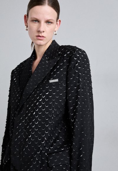 Black blazer with a textured design featuring metallic crescent shapes. Notable details include a silver logo plate on the chest pocket.