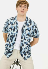 Koszula z krótkim rękawem w niebiesko-białym abstrakcyjnym wzorze, styl zapinany na guziki. Noszona na białym t-shircie, w połączeniu z jasnobeżowymi spodniami.