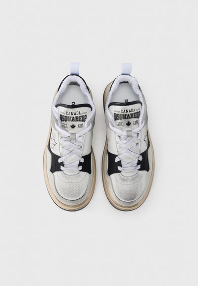 Baskets blanches et noires avec un design argenté perforé, des accents en textile, une semelle beige, et une étiquette indiquant "Canada DSQUARED2 EST 1995."
