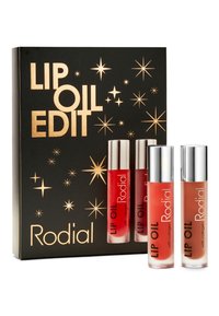 Das Rodial Lip Oil Edit Set enthält drei Lippenöle in Tuben mit silbernen Kappen, die Farben von transparent bis rot zeigen, präsentiert in einer schwarzen Schachtel mit goldener Schrift.