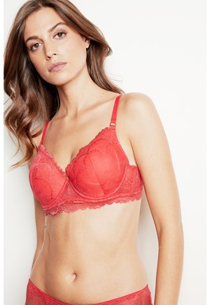Red lace bra with a scalloped design, underwire cups, adjustable straps, and patterned floral texture. Matching red lace brief visible.